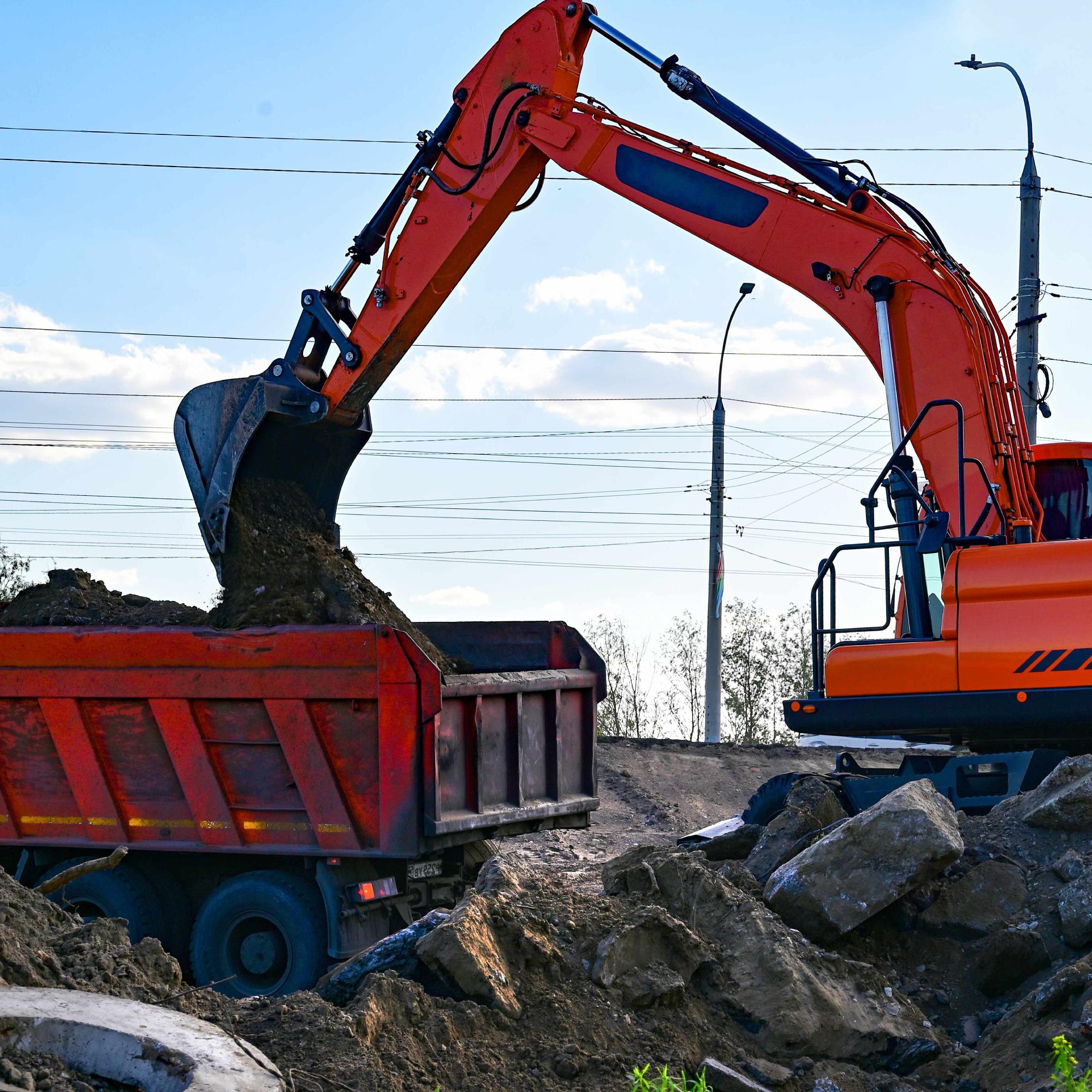 Excavator during earthmoving at open pit on blue sky background. Construction machinery and earth-moving heavy equipment for excavation, loading, lifting and hauling of cargo on job sites